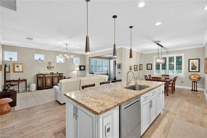 Kitchen with a chandelier, white cabinetry, light stone countertops, ornamental molding, and stainless steel dishwasher