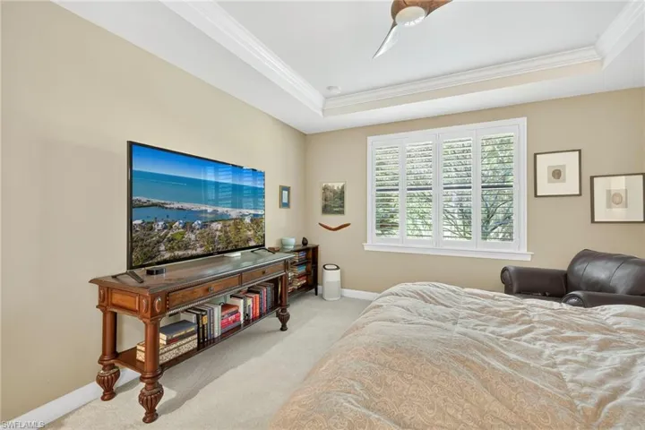 Carpeted bedroom with ornamental molding, a tray ceiling, and a ceiling fan