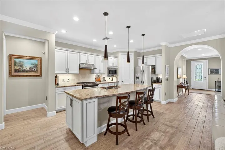 Kitchen with decorative backsplash, arched walkways, a kitchen bar, light stone countertops, and white cabinetry