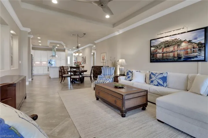 Living area with a raised ceiling, crown molding, recessed lighting, a chandelier, and a ceiling fan