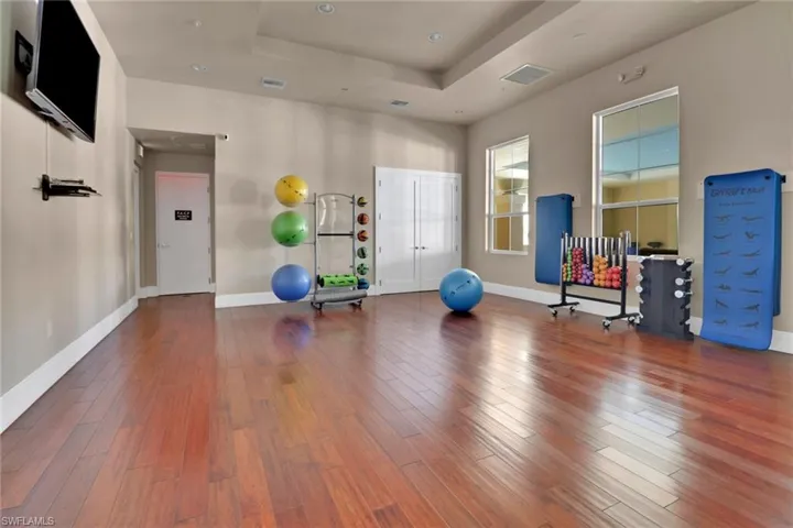 Exercise area featuring a raised ceiling, wood finished floors, and recessed lighting