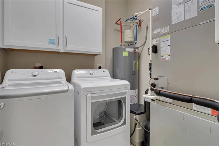 Laundry room featuring heating unit, electric water heater, washer and dryer, and cabinet space