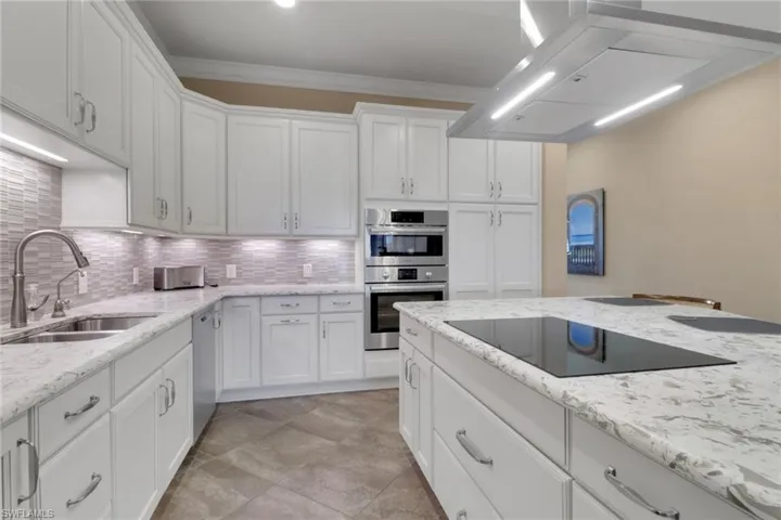 Kitchen featuring exhaust hood, white cabinets, decorative backsplash, light stone counters, and crown molding