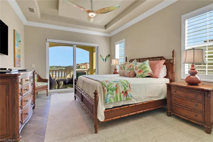 Primary Bedroom with access to exterior, a ceiling fan, a raised ceiling, and ornamental molding