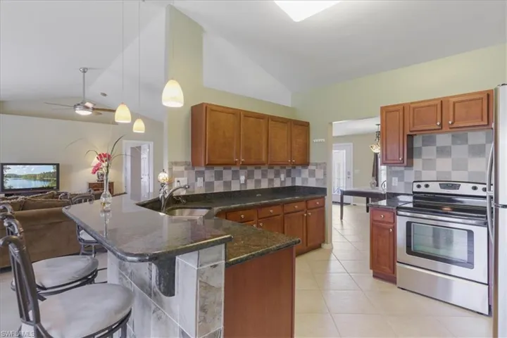 Kitchen featuring stainless steel range with electric stovetop, a sink, decorative backsplash, a peninsula, and lofted ceiling
