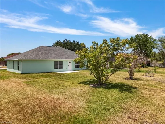 Back of house featuring a yard, a shingled roof, stucco siding, and a patio area