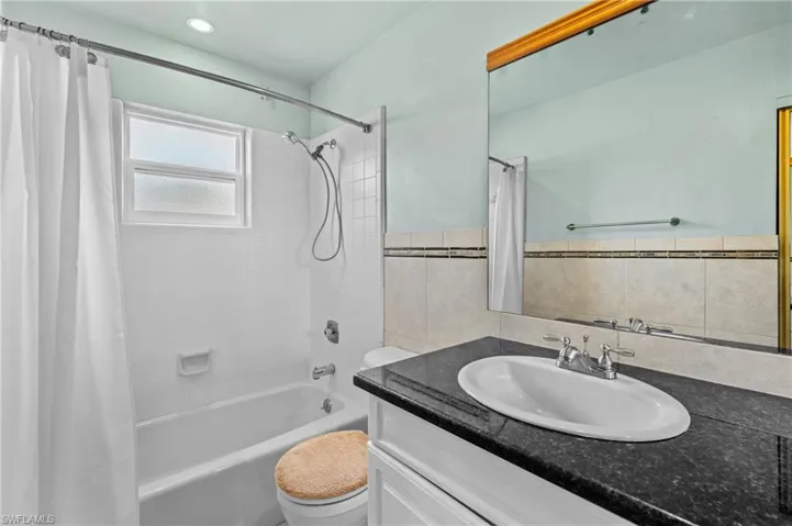 Bathroom featuring toilet, vanity, tile walls, wainscoting, and shower / bath combo with shower curtain