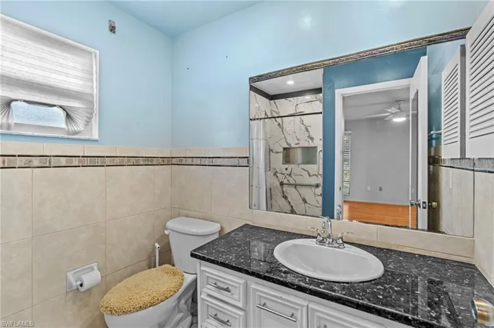 Full bath with a ceiling fan, toilet, curtained shower, vanity, and tile walls