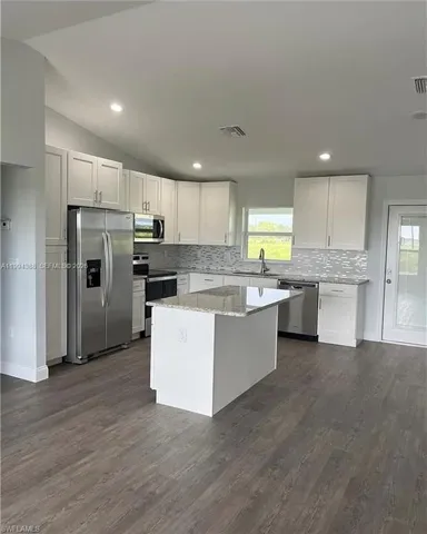 Modern kitchen with wood-finish flooring, white cabinetry, and stainless steel appliances