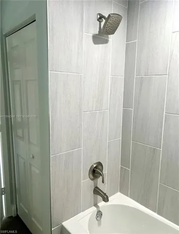 Bathtub with light gray vertical plank tile surround, brushed nickel showerhead, and matching faucet with diverter