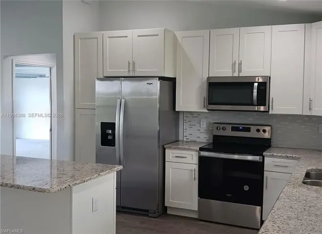 Modern kitchen featuring white shaker cabinetry, stainless steel appliances, speckled stone countertops, a tile backsplash, and an island with bar seating