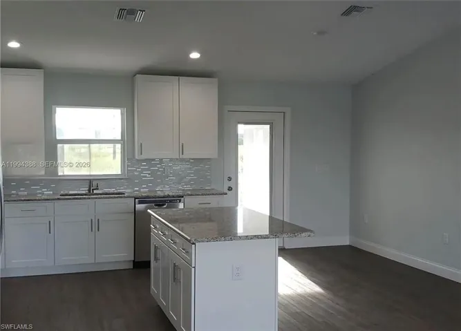Modern kitchen featuring white cabinetry, granite countertops, a tile backsplash, and stainless steel appliances