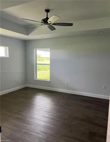 Spacious room featuring a tray ceiling, a ceiling fan with light, recessed lighting, and wood-finish flooring