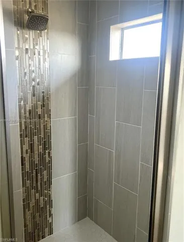 Tiled shower enclosure featuring a mosaic accent strip, rain showerhead, small transom window, and hexagonal floor tiling