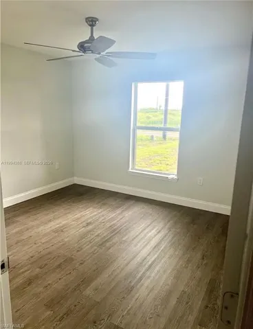 Room featuring wood-finish flooring, a ceiling fan with integrated lighting, and a window with white trim
