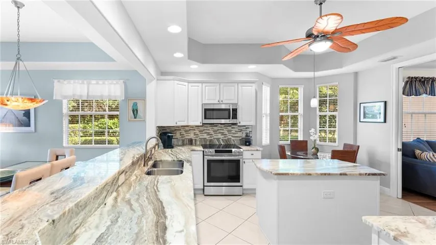 Kitchen featuring a raised ceiling, white cabinetry, light stone counters, and appliances with stainless steel finishes