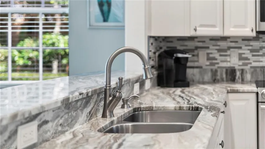 Kitchen with tasteful backsplash, white cabinetry, sink, and light stone countertops