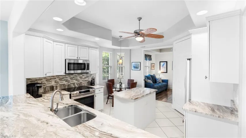 Kitchen featuring light stone counters, stainless steel appliances, a tray ceiling, sink, and white cabinets