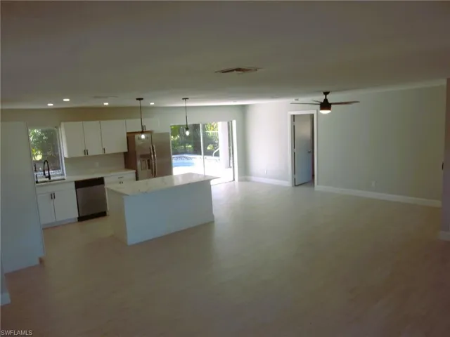 Kitchen with open floor plan, decorative light fixtures, stainless steel appliances, white cabinets, and a center island