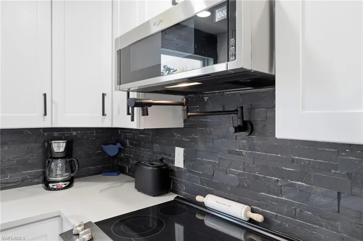Kitchen featuring stainless steel microwave, pot filler, white cabinets, decorative backsplash, light stone countertops, and black electric range