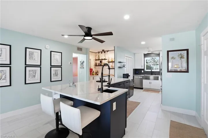 Kitchen with a ceiling fan, a breakfast bar, a center island with sink, dishwasher, and light quartz counters