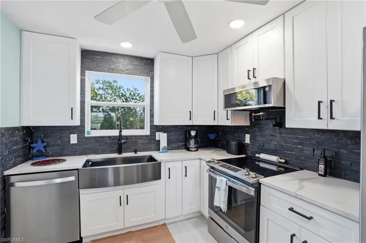 Kitchen with stainless steel appliances, white cabinets, light stone counters, ceiling fan, and tasteful backsplash
