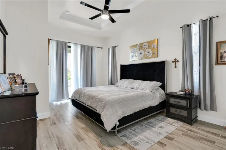 Bedroom with baseboards, a tray ceiling, and light wood-type flooring