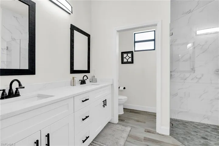 Bathroom featuring toilet, a sink, a marble finish shower, and baseboards