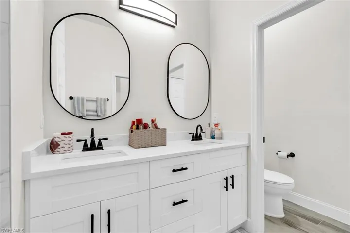 Bathroom featuring baseboards, a sink, double vanity, and toilet