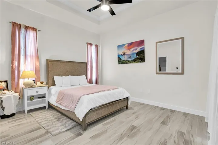 Bedroom with baseboards, light wood-style flooring, a tray ceiling, and ceiling fan