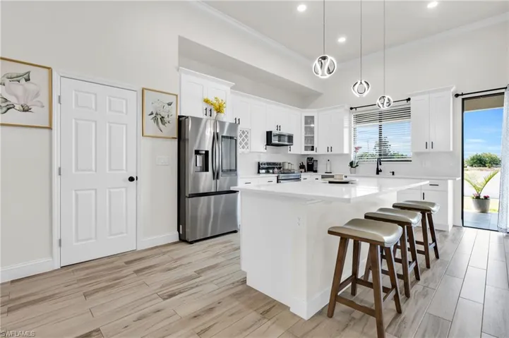 Kitchen with light wood finished floors, ornamental molding, a kitchen island, and appliances with stainless steel finishes