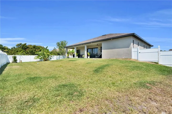Back of house with ceiling fan, a lawn, a fenced backyard, and stucco siding