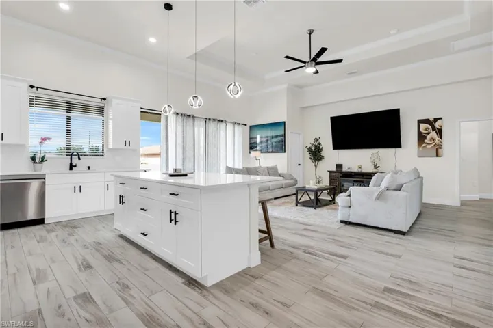 Kitchen with stainless steel dishwasher, a tray ceiling, a sink, open floor plan, and crown molding
