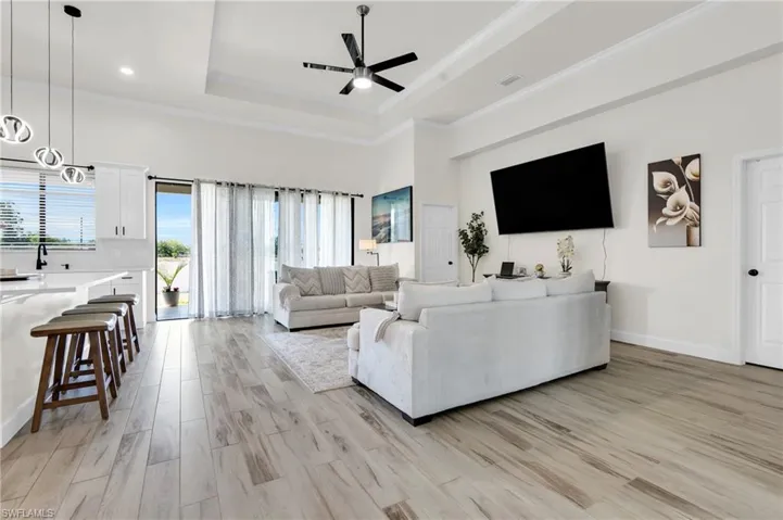 Living area with ornamental molding, a tray ceiling, light wood-style floors, and ceiling fan