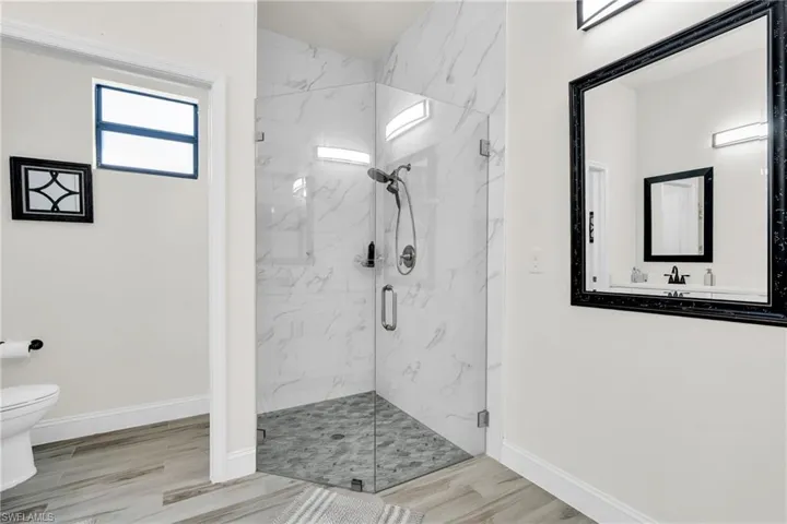 Bathroom with wood finished floors, baseboards, a marble finish shower, and toilet