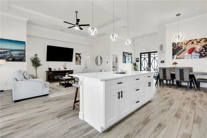 Kitchen with ceiling fan with notable chandelier, open floor plan, light wood-style floors, and crown molding