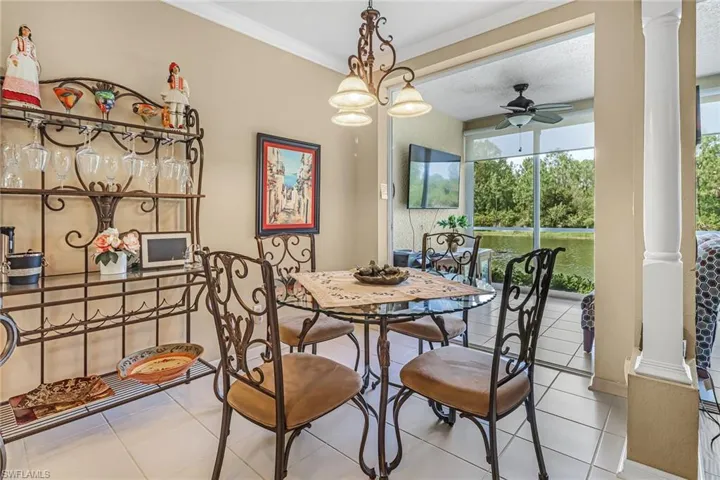 Dining room with crown molding, light tile flooring, ornate columns, and ceiling fan with notable chandelier