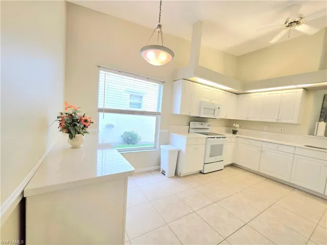Kitchen featuring white appliances, white cabinets, pendant lighting, and light tile patterned flooring