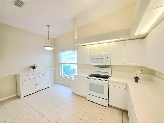 Kitchen with white appliances, light countertops, white cabinets, lofted ceiling, and light tile patterned floors