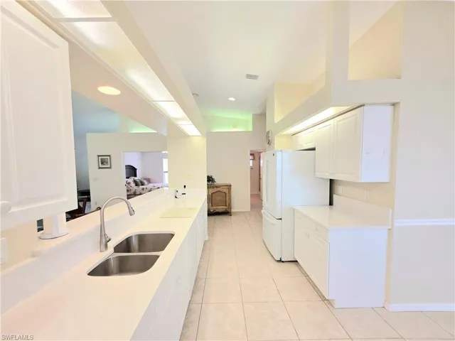 Kitchen featuring light tile patterned flooring, white cabinetry, freestanding refrigerator, and light stone countertops