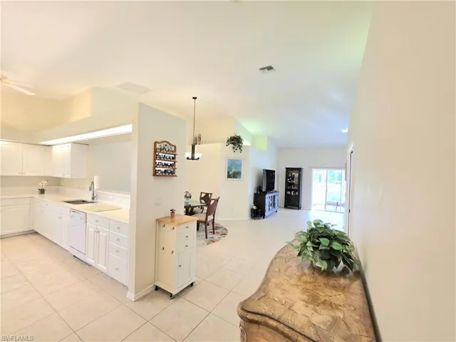 Kitchen with light countertops, light tile patterned flooring, white cabinetry, decorative light fixtures, and white dishwasher