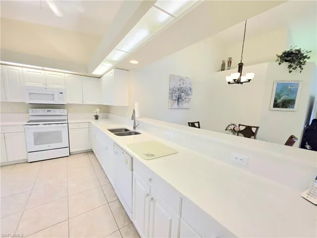 Kitchen featuring white appliances, white cabinetry, light tile patterned floors, decorative light fixtures, and light stone counters