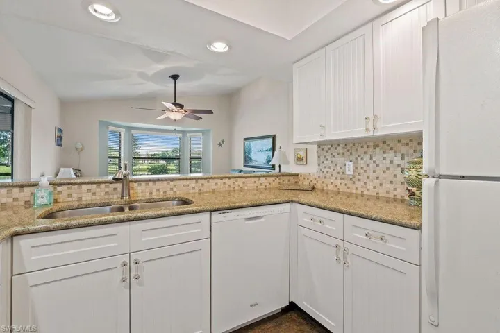 Kitchen with sink, white appliances, decorative backsplash, and light stone counters