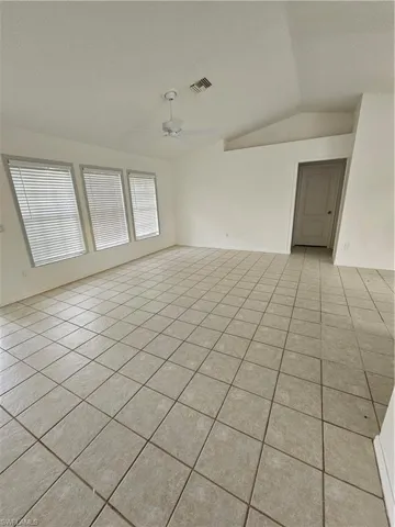 Empty room with vaulted ceiling, light tile patterned flooring, and ceiling fan