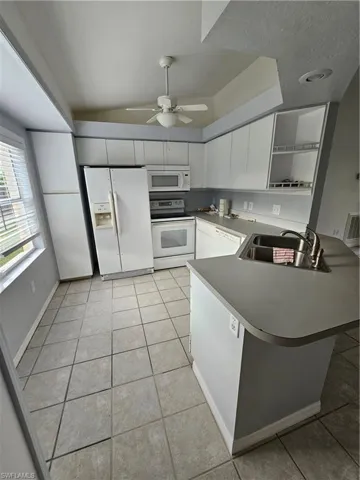 Kitchen featuring white appliances, light tile patterned floors, kitchen peninsula, sink, and ceiling fan