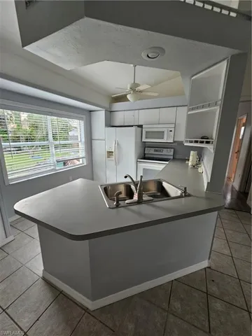Kitchen with white cabinetry, stove, kitchen peninsula, sink, and ceiling fan