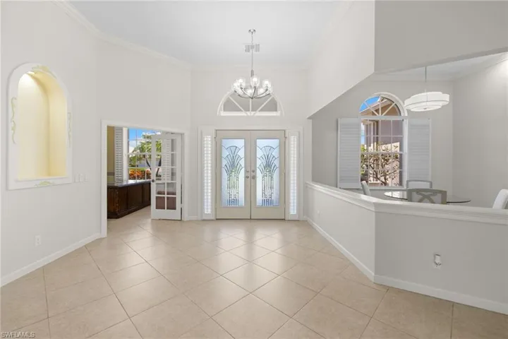 Grand entry foyer featuring double doors with decorative glass panels, an arched transom window, and a high vaulted ceiling