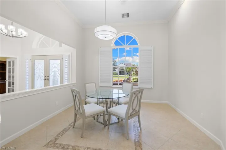 Dining area featuring a large arched window with plantation shutters, a contemporary pendant light fixture, and tile flooring with decorative inlay