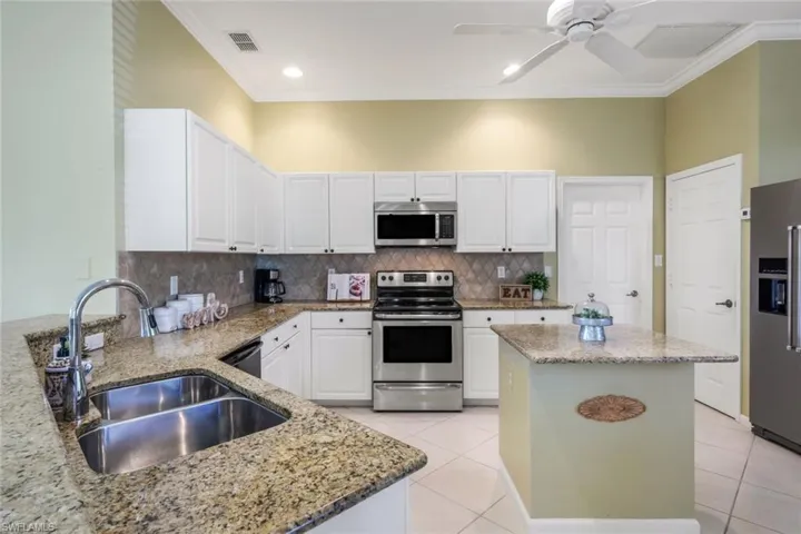 Kitchen featuring sink, white cabinetry, appliances with stainless steel finishes, a kitchen island, and light stone countertops