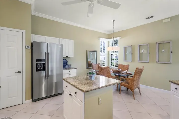 Kitchen with light tile patterned floors, white cabinetry, a center island, stainless steel refrigerator with ice dispenser, and decorative light fixtures